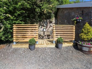 A wooden bench with a table and chairs, potted plants, a stone wall, and a hanging flower basket.