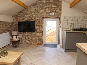 A kitchen with a stone wall, a television, and a door leading outside.