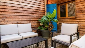 A wooden cabin with a blue door, a sofa, a table, and a potted plant. - Chalet Jardin Les Fées (Saint-Remèze)