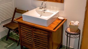 A bathroom with a wooden vanity, a large mirror, a white sink, and a small round table with towels. - Chalet Jardin Les Fées (Saint-Remèze)