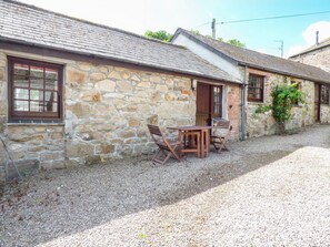 A stone building with a gravel driveway, a wooden table and chairs, and a window with a wooden shutter. - The Bullshed, Marazion (Hayle)