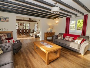 Ein Wohnzimmer mit Couchtisch aus Holz, grauen Sofas und einem Essbereich mit Tisch und Stühlen.