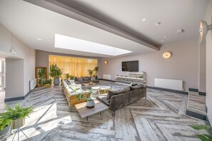 Un vaste espace de vie comprenant un grand canapé, une table basse et un téléviseur. On y trouve également des plantes en pot et un plancher en bois.