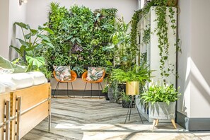 Une pièce comprenant un lit, deux chaises, une plante en pot, un mur végétal et un sol carrelé.