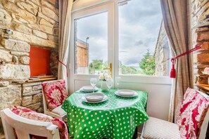 Ein Essbereich mit Steinwand, Tisch mit grüner Tischdecke, weißen Tellern und Stühlen mit blumigen Kissen.