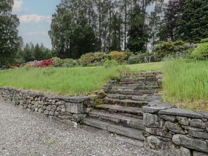 A stone staircase leading up a grassy slope, surrounded by a stone wall and dense trees. - West Cottage, Comrie (Crieff)