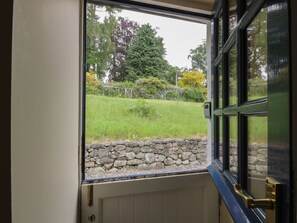 An open door with a view of a stone wall and a grassy area with trees. - West Cottage, Comrie (Crieff)