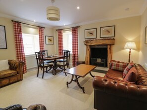 A living room with a fireplace, a dining table with chairs, a sofa, and a lamp. - West Cottage, Comrie (Crieff)