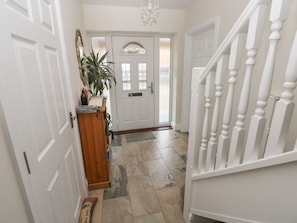 A hallway with a white door, a potted plant, a wooden cabinet, and a white staircase.