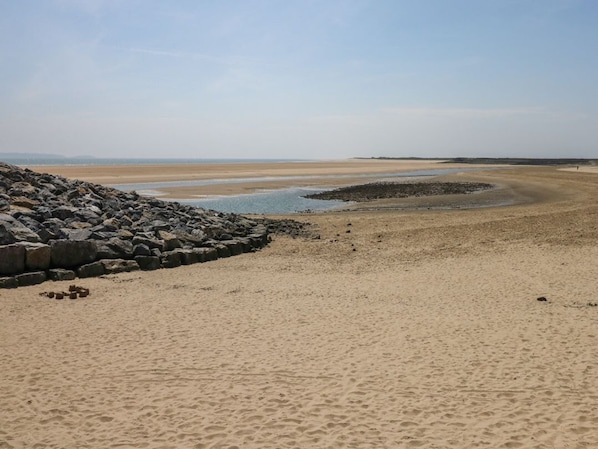 A beach with a rocky breakwater, sandy shore, and calm water.