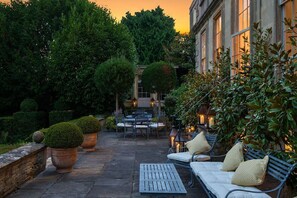 An outdoor patio with a table and chairs, surrounded by potted plants and a stone wall. - Batheaston House, Batheaston (BATH)