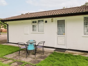 Un bâtiment d’un seul étage, doté d’un toit en tuiles, d’une façade blanche et d’un petit patio avec une table et des chaises.
