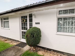 Un bâtiment blanc avec une porte, des fenêtres et un petit arbuste devant.