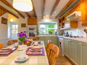 A kitchen with wooden cabinets, a dining table set with plates, cups, and a vase of flowers. - Townfoot Cottage, Elsdon (Newcastle upon Tyne)