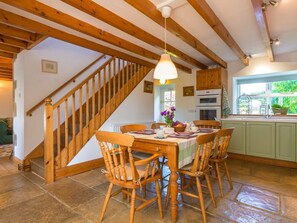 A dining area with a wooden table and chairs, a hanging light fixture, a staircase, and a view of the outdoors through a window. - Townfoot Cottage, Elsdon (Newcastle upon Tyne)