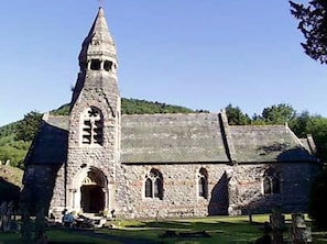 Una iglesia de piedra con una torre alta, ventanas en arco y un patio cubierto de césped.
