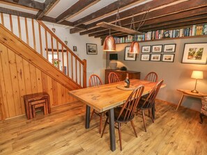 A wooden dining table with chairs, a staircase, and a bookshelf with books.
