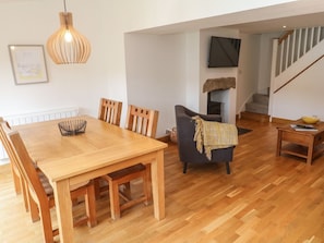 A dining area with a wooden table and chairs, a sofa, a television mounted on the wall, and a staircase in the background. - Charming Anneth Lowen Retreat (Hayle)