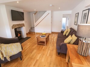 A living room with a fireplace, sofa, coffee table, and a TV mounted on the wall. - Charming Anneth Lowen Retreat (Hayle)