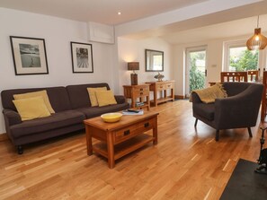 A living room with a sofa, armchair, wooden coffee table, and a dining area with a table and chairs. - Charming Anneth Lowen Retreat (Hayle)