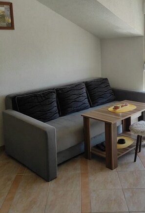 Ein modernes Wohnzimmer mit einem grauen Sofa, einem Holztisch und einem kleinen runden Tisch mit gelbem Fuß.