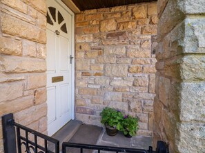 A stone building with a white door, a small porch, and potted plants. - Vive House, Ribchester (Preston)