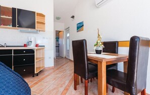 Une pièce compacte comprenant un coin cuisine, une table à manger avec des chaises, un espace douche et un tableau au mur.