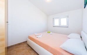 Une petite chambre avec un lit simple, une fenêtre, une porte et un sol carrelé.