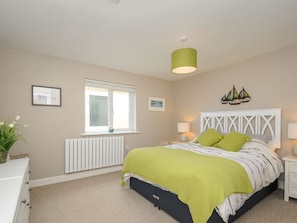 Une chambre à coucher comprenant un lit, une fenêtre, un radiateur, une lampe fixée au mur et un modèle de voilier décoratif.