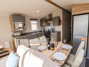 Cocina compacta con microondas, estufa y refrigerador. Hay una mesa de comedor preparada con platos y una botella de vino.