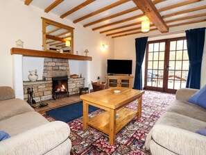 A living room with a stone fireplace, wooden beams, a television, and a patterned rug. - The Stable, Maulds Meaburn (Penrith)