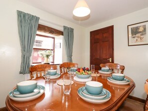 A dining room with a wooden table set for four, featuring blue and white plates and bowls, a fruit bowl, and a vase with flowers. - The Stable, Maulds Meaburn (Penrith)