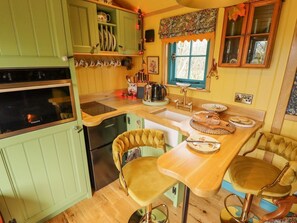 A kitchen with a wooden countertop, two chairs, a stove, and a window with a floral curtain. - Catchwater rests in Keal Cotes (Spilsby)