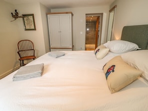 Un lit bien fait, avec des oreillers et une serviette pliée, une chaise en bois, une armoire et un miroir.