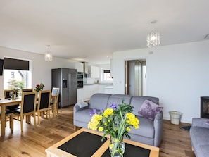 Un salon moderne avec un canapé, une table à manger et des chaises, une cuisine en arrière-plan et un vase rempli de fleurs posé sur une table basse.