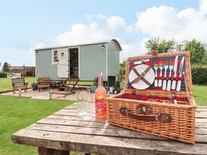 Een picknickopstelling met een rieten mand, een fles en glazen op een houten tafel.
