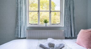 A bedroom with a bed, a radiator, a window with curtains, and a plant on the windowsill. - Grassholme, Hawkshead (Ambleside)