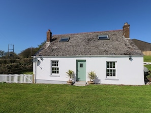 A white cottage with a green door, two windows, a chimney, and a white picket fence. - Piglet Cottage, Milford Haven. (Haverfordwest)
