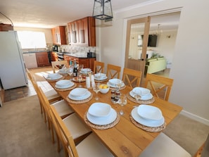 A dining area with a wooden table set for six, surrounded by wooden chairs. - Piglet Cottage, Milford Haven. (Haverfordwest)