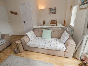 A cozy living room with a sofa, a small table, a chair, a radiator, and a door. - Ramblers Cottage, Powburn (Alnwick)