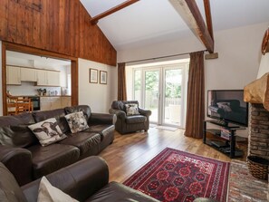 A living room with a sofa, armchairs, a TV, a fireplace, and a kitchen in the background. - The Wagon Shed: Ground Floor Retreat (Driffield)