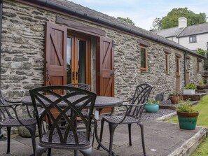 A stone building with a wooden door and windows, outdoor seating with chairs and a table, and potted plants in the garden area. - Siabod View, Betws-Y-Coed (Llanrwst)