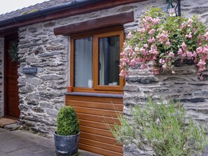 A stone building with a wooden door, a window with curtains, and a hanging flower basket. - Siabod View, Betws-Y-Coed (Llanrwst)
