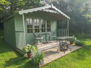 Eine kleine, grüne Holzhütte mit Veranda, Tisch und Stühlen.