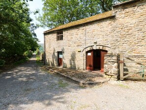 Un edificio de piedra con un sendero de grava que conduce a él, puertas de madera y un muro de piedra.