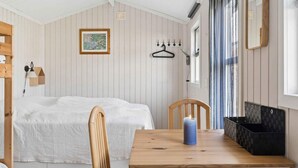 Ein Zimmer mit einem Bett, einem Holztisch mit Kerze, einem Stuhl, einem Kleiderständer und einem Fenster mit Vorhängen.