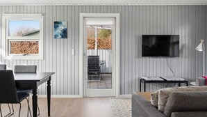 Ein modernes Wohnzimmer mit Essbereich, einem an der Wand montierten Fernseher und Blick durch eine Glastür auf eine Terrass'.