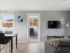 Ein modernes Wohnzimmer mit Essbereich, einem an der Wand montierten Fernseher und Blick durch eine Glastür auf eine Terrass'.