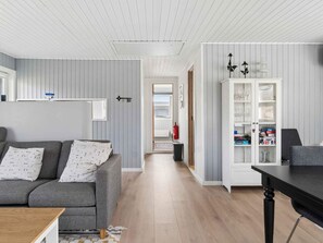 Ein modernes Wohnzimmer mit grauem Sofa, einem Holztisch und einer weißen Kommode mit Glaswaren.