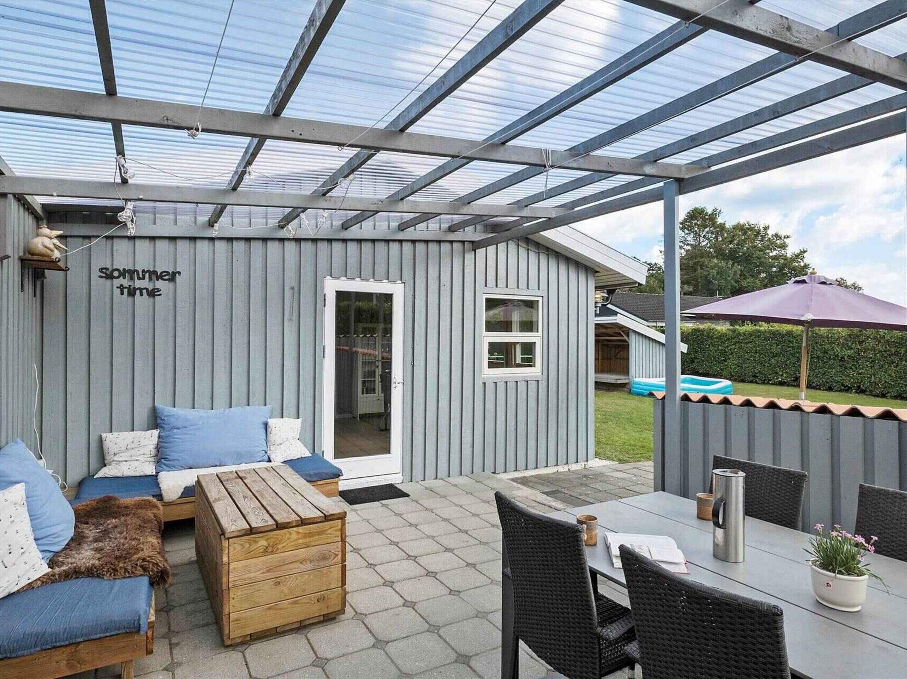 Un patio couvert comprenant un banc en bois, une table avec des chaises et une porte vitrée.